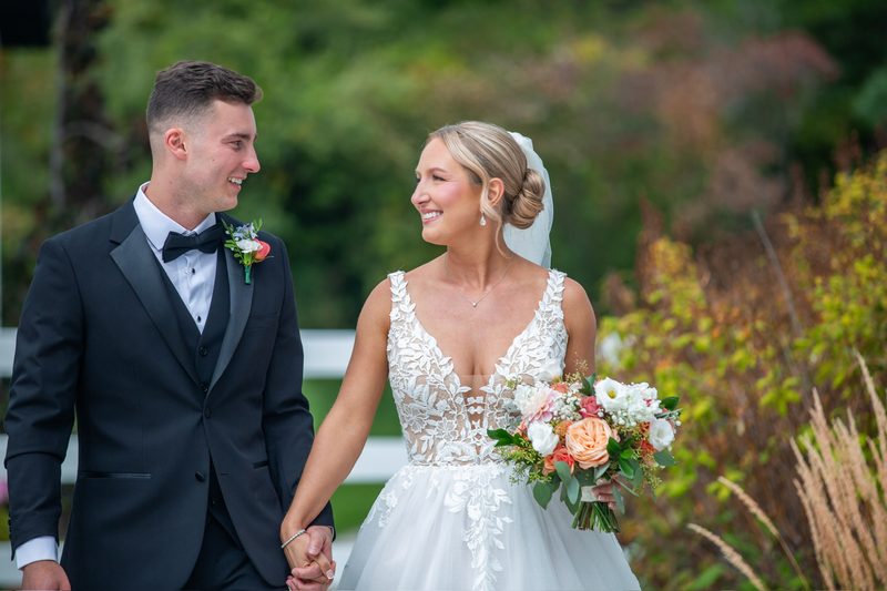 Bride and groom walking hand in hand, bride holding a peach bouquet