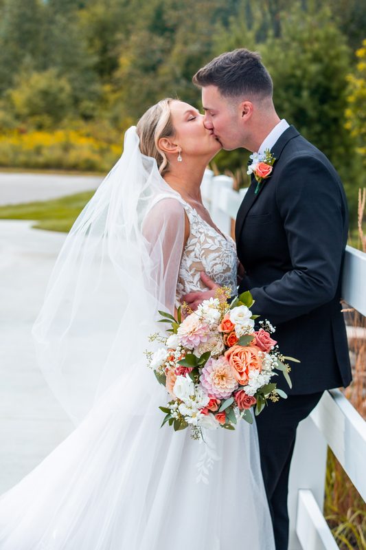 Bride and groom kissing, peach bouquet in hand