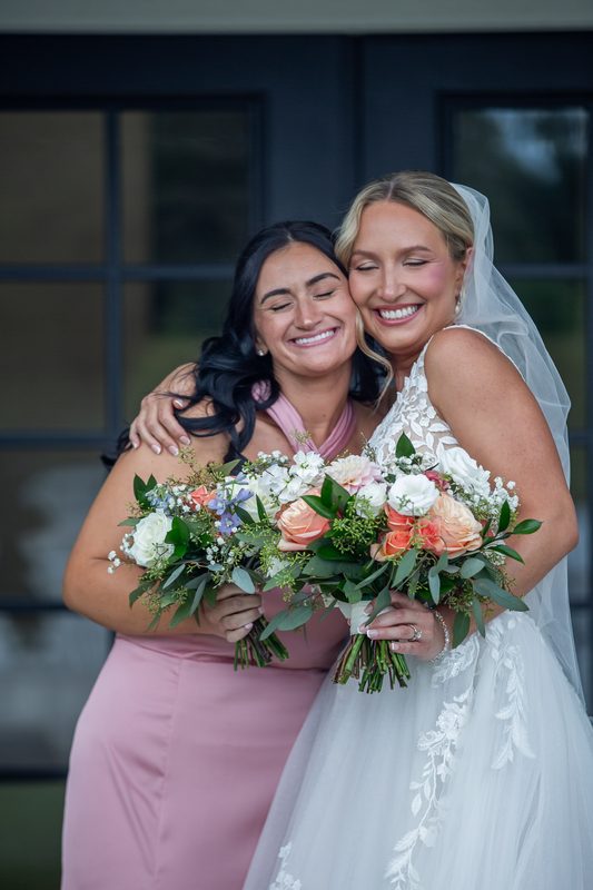 Bride and bridesmaid laughing with their bouquets