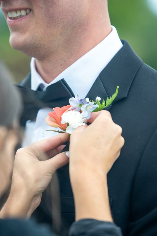 Pinning a peach rose boutonniere on a groom's lapel
