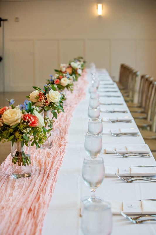 Long reception table with peach runner and small floral arrangements